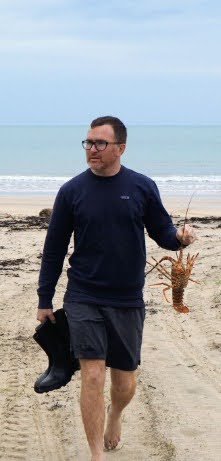 Ian holding a crayfish on the beach.