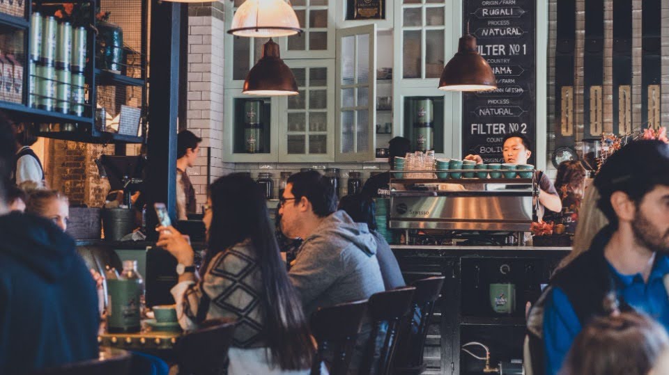 A busy cafe, a man checking his phone at a crowded table.